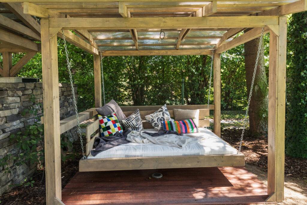 Rocking bed pergola. Garden bed with pillows a porch swing daybed with colorful covers an a shady backyard garden