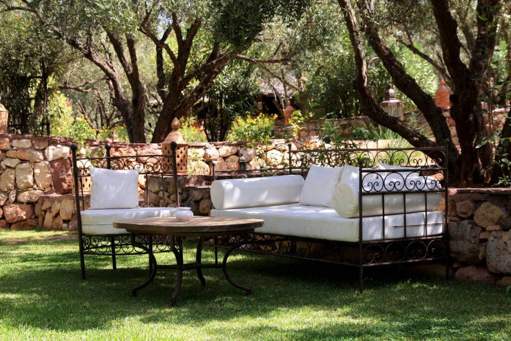 salon de jardin en fer forgé a shady patio with beautiful seating, the sofa and armchair cushions in protective covers in ivory color