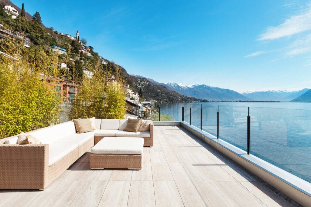 modern architecture, beautiful terrace penthouse patio with large outdoor seating area. A rattan sofa has white cushion covers on it. A stunning sea view.