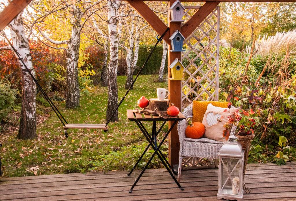 Piękna jesień w ogrodzie na tarasie warm autumn in the garden, seating area with pillows and a whimsical centerpiese of colorful birdhouses