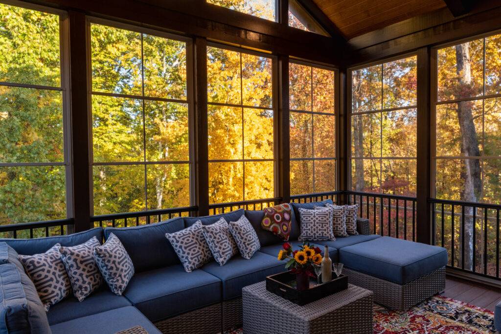 Cozy Porch Enclosure in Early Morning Rain Cozy screened porch with decorated seating area in early morning, rain drops on window and autumn leaves and woods in the background.