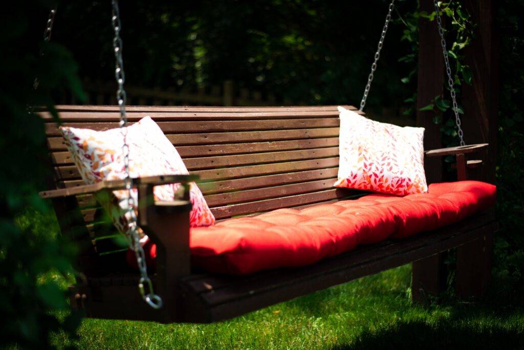 Hanging wooden bed swing with pillows in the garden lovely porch swing decorated with seating cushion in red and two pillows