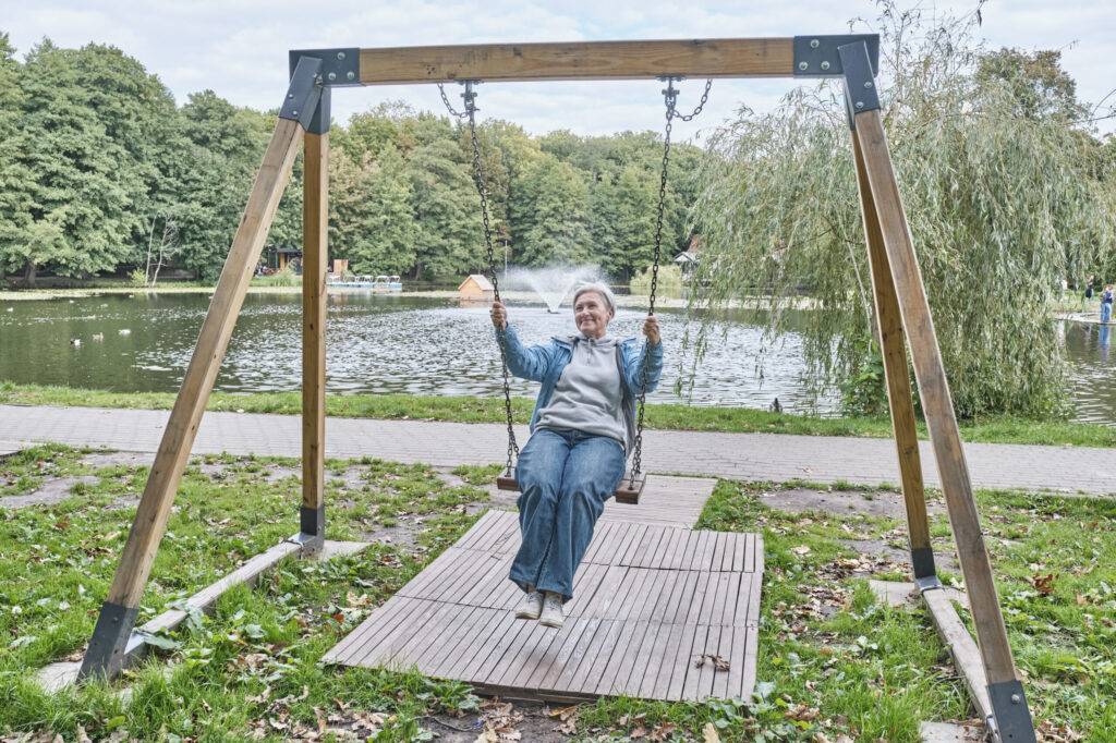 Happy senior caucasian woman with short gray hair swinging on chain swing in park